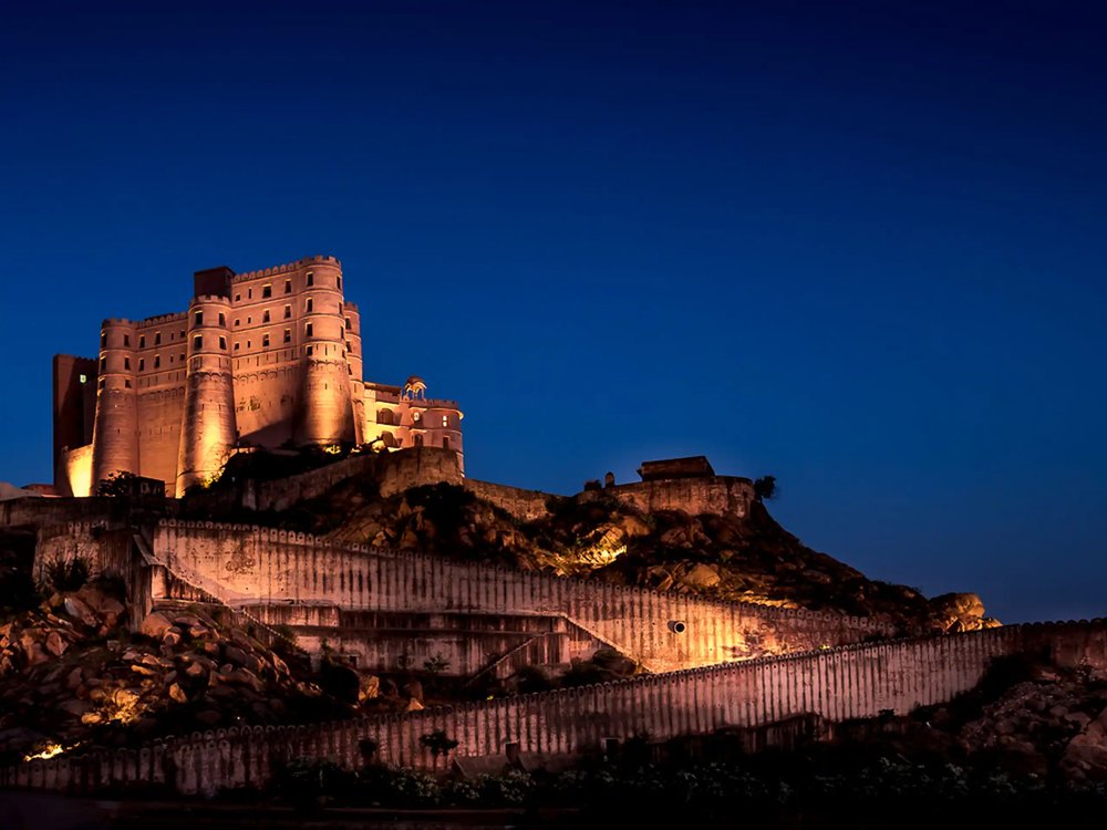 Alila Fort Bishangarh lit against a deep blue sky, its ramparts running down the granite hill